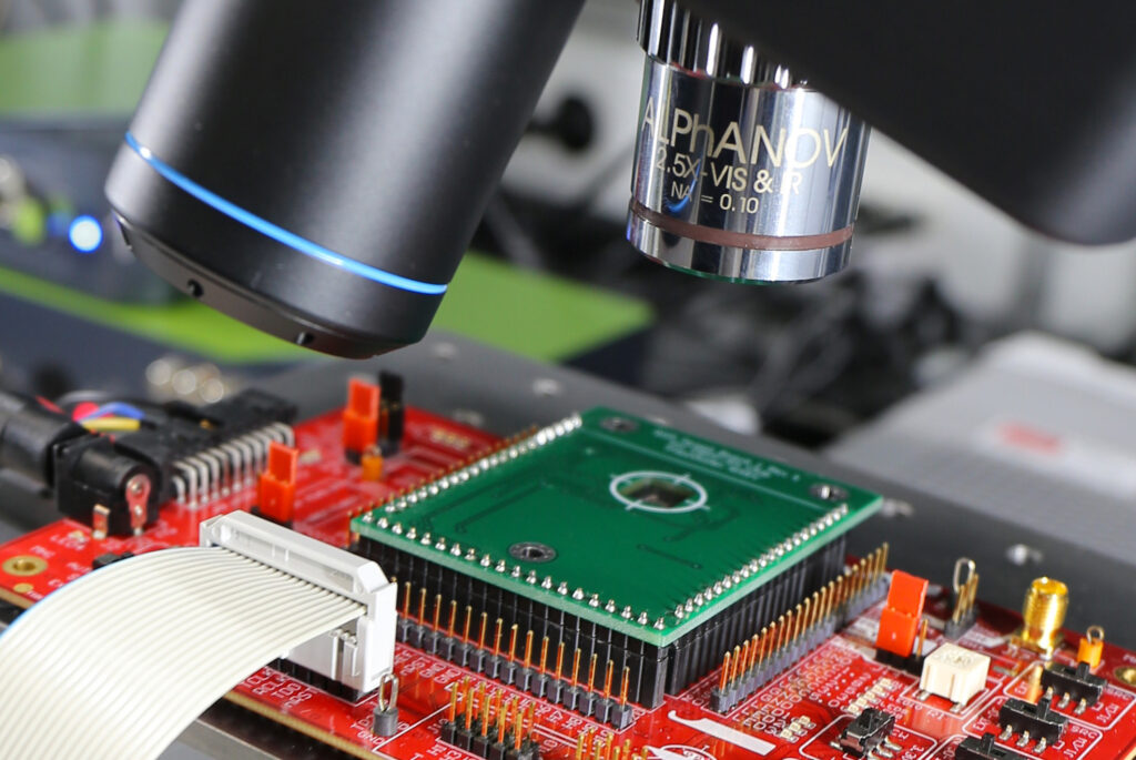 Ein Objektiv des Laseraufbaus steht über einer Testplatine mit einem Target Chip.